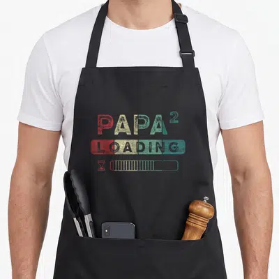 Tablier de cuisine noir avec inscription Papa 2 Loading et barre de progression multicolore sur le devant.