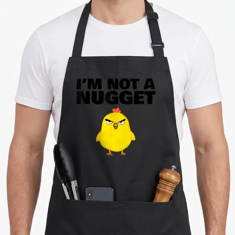 Tablier de cuisine noir avec un poussin jaune et le texte I'm Not a Nugget en lettres noires audacieuses.