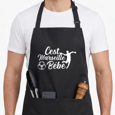 Tablier de cuisine noir avec inscription C'est Marseille Bébé, silhouette footballeur et ballon blanc.
