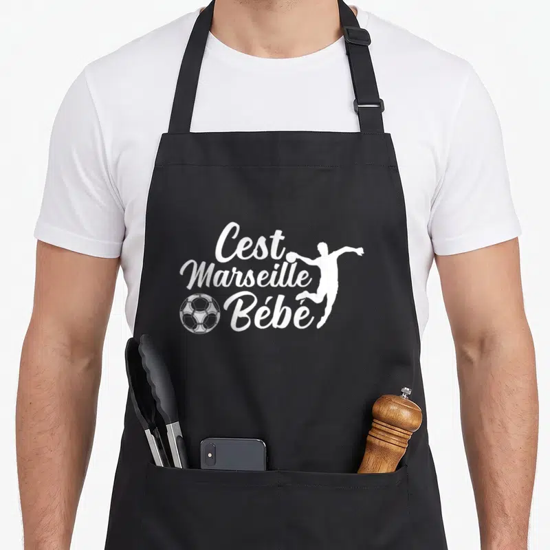 Tablier de cuisine noir avec inscription C'est Marseille Bébé, silhouette footballeur et ballon blanc.