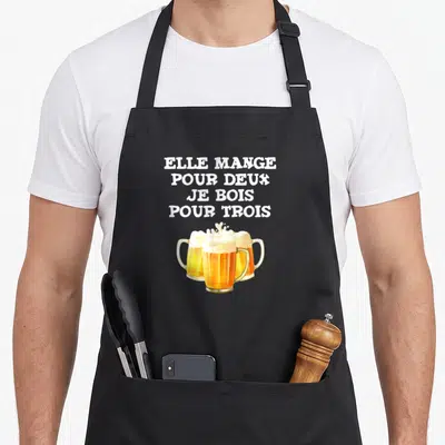 Tablier de cuisine noir avec inscription Elle mange pour deux je bois pour trois et trois verres de bière dorée.