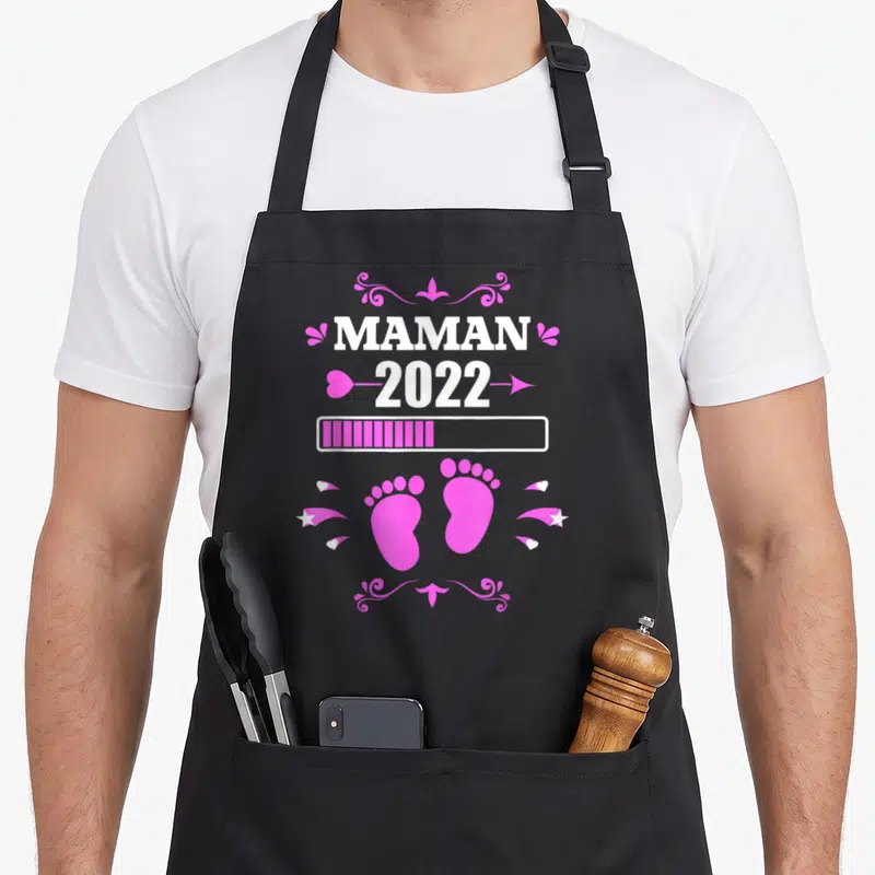 Tablier de cuisine noir avec inscription Maman 2022, barres de progression et silhouettes de petits pieds roses ornés d'étoiles.