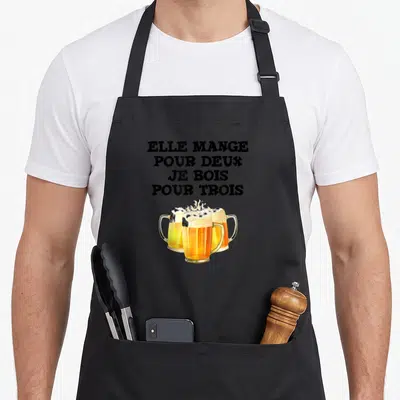 Tablier de cuisine noir avec trois verres de bière et le texte elle mange pour deux je bois pour trois imprimé en noir.