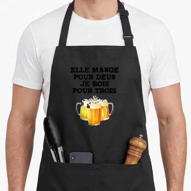 Tablier de cuisine noir avec trois verres de bière et le texte elle mange pour deux je bois pour trois imprimé en noir.