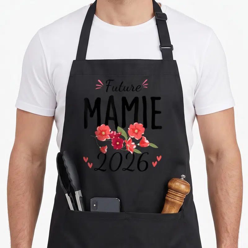 Tablier de cuisine noir avec inscription Future Mamie 2026 et bouquet de fleurs roses et rouges.