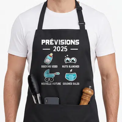 Tablier de cuisine noir avec illustration colorée annonçant prévisions 2025 biberons vides nuits blanches nouvelle voiture et couches sales.