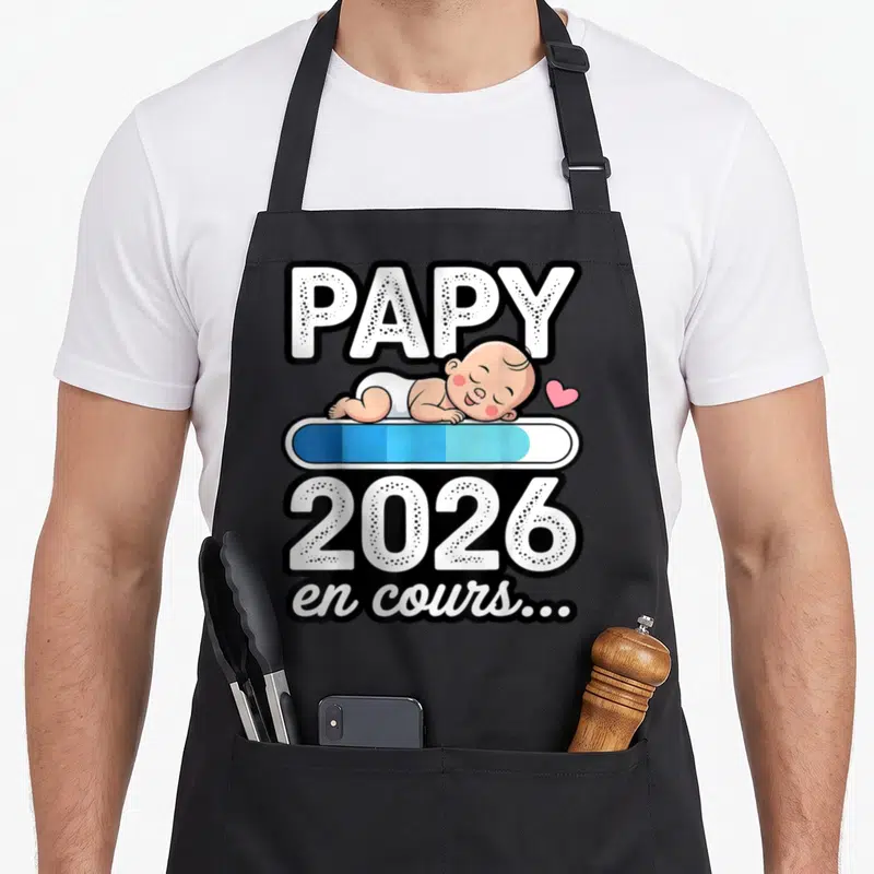 Tablier de cuisine noir avec inscription Papy 2026 en cours et illustration d'un bébé dormant sur une barre de progression.