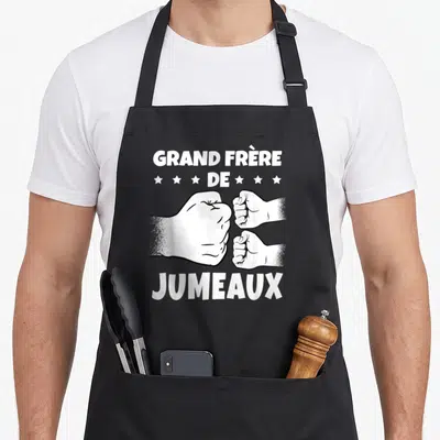 Tablier de cuisine noir avec illustration de trois poings se touchant et texte blanc announcing grand frère de jumeaux.