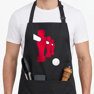 Tablier de cuisine noir avec trois silhouettes rouges de joueurs de baby-foot alignés et une balle blanche en bas à droite.