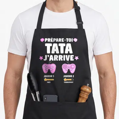 Tablier de cuisine noir avec texte blanc Prépare-toi Tata J'arrive et deux manettes roses Joueur 1 et Jouleur 2.
