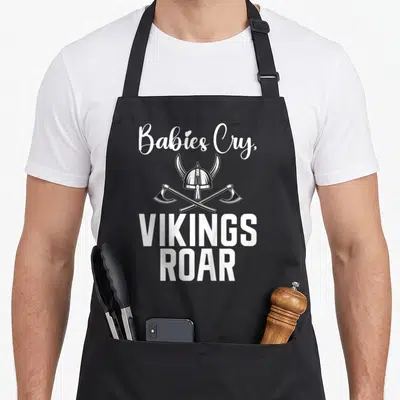 Tablier de cuisine noir avec inscription « Babies Cry, VIKINGS ROAR » et casque viking croisé d'axes.