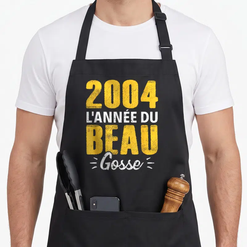 Tablier de cuisine noir avec le texte 2004 l'année du beau gosse en typographie jaune et blanche.