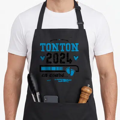 Tablier de cuisine noir avec inscription Tonton 2024 en cours et empreintes de pieds bleues.