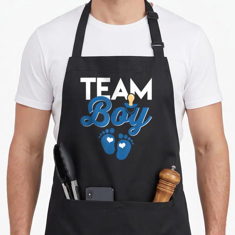 Tablier de cuisine noir avec l'inscription Team Boy en bleu, des empreintes de pieds de bébé et un doudou jaune.