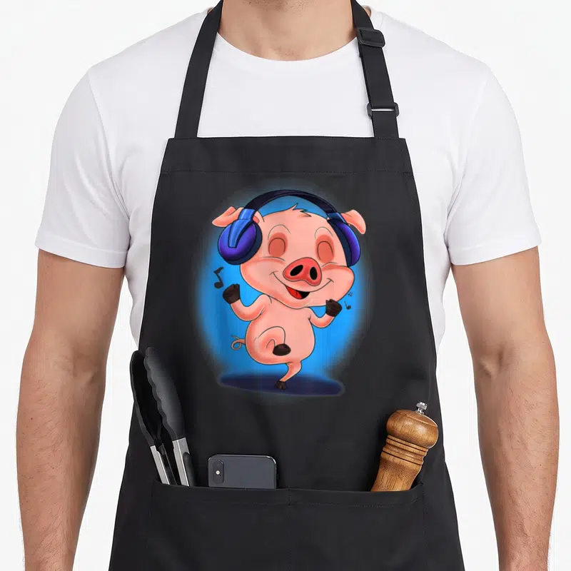 Tablier de cuisine noir avec illustration colorée d'un porcelet dansant avec un casque DJ bleu sur fond lumineux.