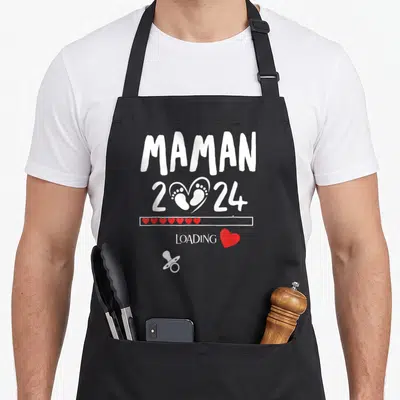 Tablier de cuisine noir avec inscription Maman 2024 Loading et icônes de pieds de bébé et sucette blanche.