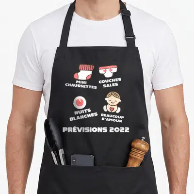 Tablier de cuisine noir avec illustration humoristique sur la grossesse et les prévisions 2022 incluant un bébé et des chaussettes.