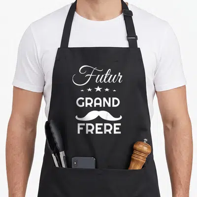 Tablier de cuisine noir avec inscription Futur Grand Frère, étoiles et moustache blanche stylisée.