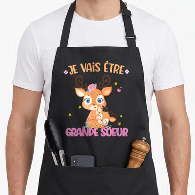 Tablier de cuisine noir avec illustration d'un cerf orange et du texte Je vais être grande sœur en lettres colorées.