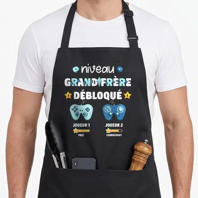 Tablier de cuisine noir avec niveau grand frère débloqué et deux manettes de jeu vidéo colorées.