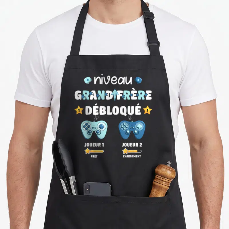 Tablier de cuisine noir avec niveau grand frère débloqué et deux manettes de jeu vidéo colorées.
