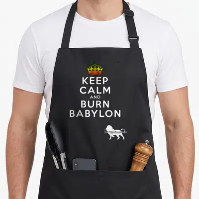 Tablier de cuisine noir avec inscription Keep Calm and Burn Babylon, couronne colorée et silhouette de lion blanc en bas à droite.