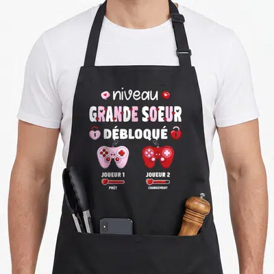 Tablier de cuisine noir avec manettes roses et rouges et texte Grande Soeur Débloqué