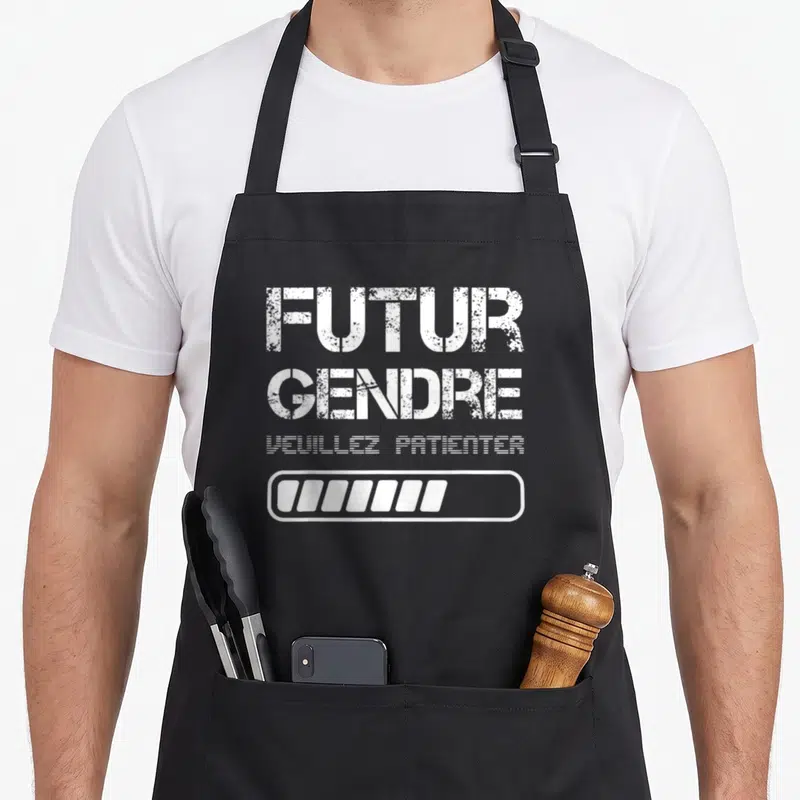 Tablier de cuisine noir avec inscription Futur Gendre Veuillez Patienter et barre de progression blanche en bas du motif central.