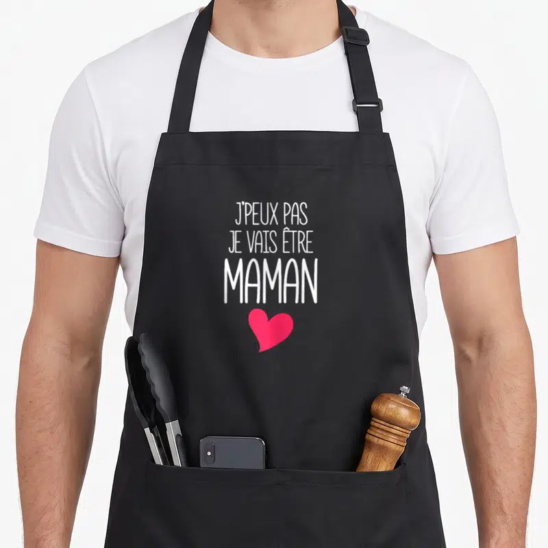 Tablier de cuisine noir avec l'inscription J'peux pas je vais être maman et un cœur rose en dessous.