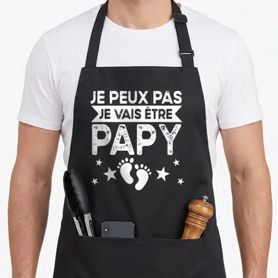 Tablier de cuisine noir avec inscription Je peux pas je vais être papy et deux petits pieds blancs entourés d'étoiles.