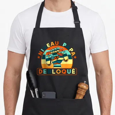 Tablier de cuisine noir avec une main tenant une manette et le texte Niveau Papa Débloqué en couleurs rétro.