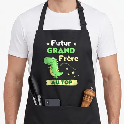Tablier de cuisine noir avec illustration T-Rex vert et texte Futur Grand Frère Au Top entouré d'étoiles jaunes.