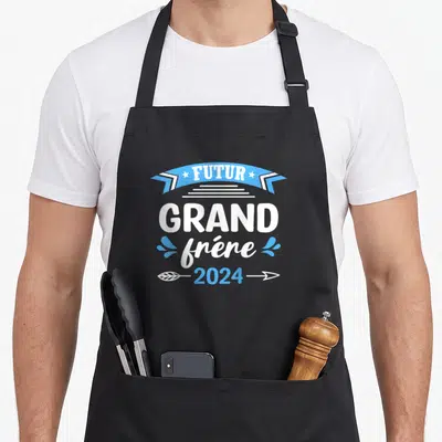 Tablier de cuisine noir avec le texte Futur Grand Frère 2024 en bleu et blanc sur fond uni.
