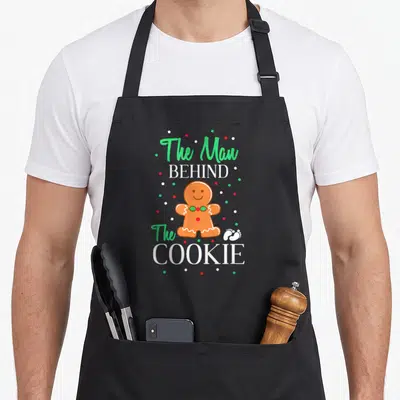 Tablier de cuisine noir avec un biscuit en pain d'épice et le texte The Man Behind The Cookie.