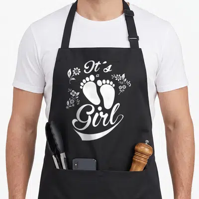 Tablier de cuisine noir avec empreintes de pieds blancs, fleurs et texte It's a Girl Rose.
