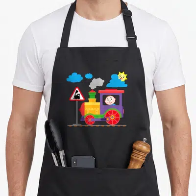 Tablier de cuisine noir avec locomotive colorée et bébé conducteur au volant.