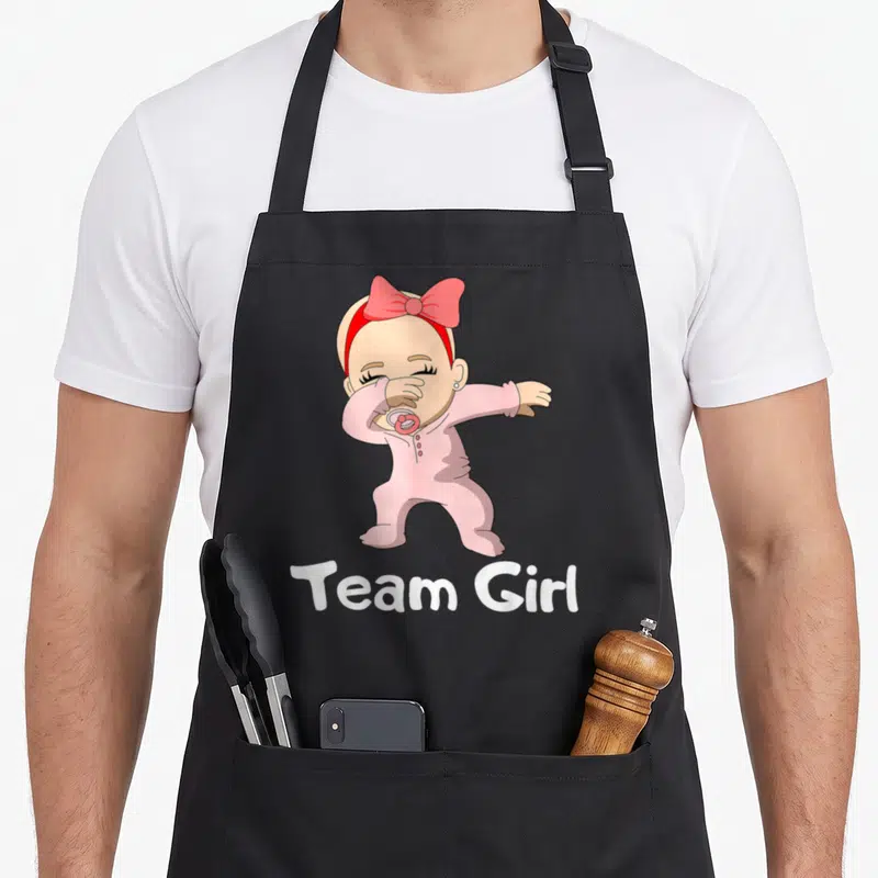 Tablier de cuisine noir avec un bébé rose effectuant la pose dab et le texte Team Girl en bas.