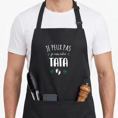 Tablier de cuisine noir avec texte blanc Je peux pas je vais être Tata future et motifs de petits pieds et cœurs turquoise.