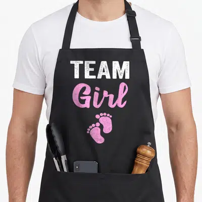Tablier de cuisine noir avec l'inscription Team Girl et deux empreintes de petits pieds roses en bas du motif imprimé.