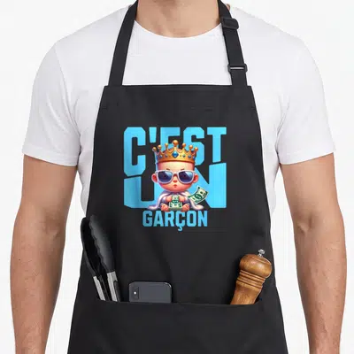 Tablier de cuisine noir avec illustration d'un bébé roi en lunettes de soleil tenant des billets devant l'inscription C'est un garçon.
