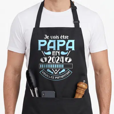 Tablier de cuisine noir avec annonce Je vais être papa en 2024 et Veuillez patienter en bleu ciel et blanc.