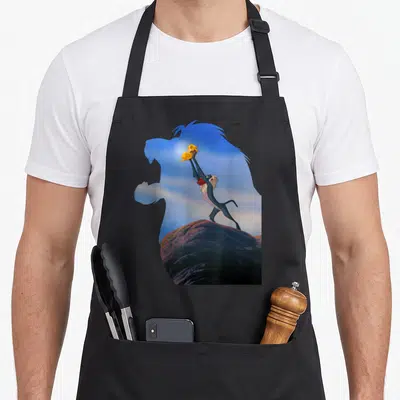 Tablier de cuisine noir avec Rafiki levant Baby Simba sur un rocher en silhouette de lion.