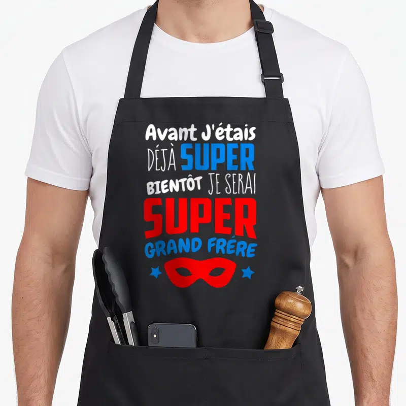 Tablier de cuisine noir avec texte blanc bleu rouge et masque super-héros pour future grande fratrie.