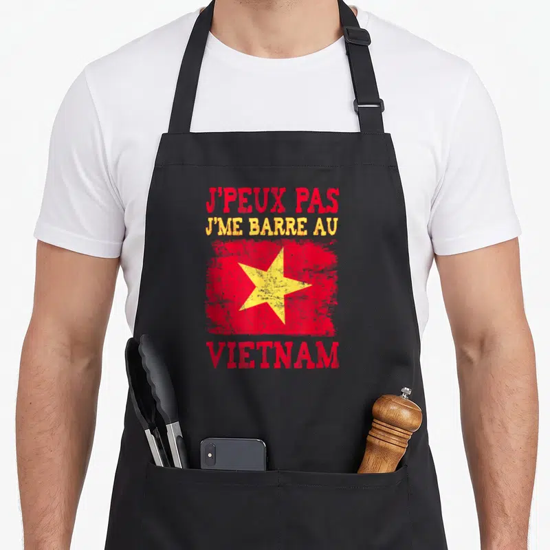 Tablier de cuisine noir avec inscription rouge et jaune J'peux pas j'me barre au Vietnam sur fond de drapeau stylisé.