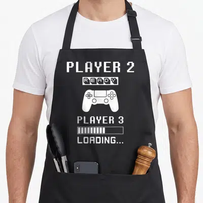 Tablier de cuisine noir avec illustration manette et texte Player 2 Ready chargement grossesse style pixel art blanc.