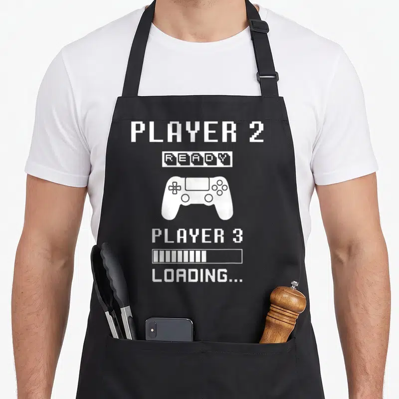 Tablier de cuisine noir avec illustration manette et texte Player 2 Ready chargement grossesse style pixel art blanc.