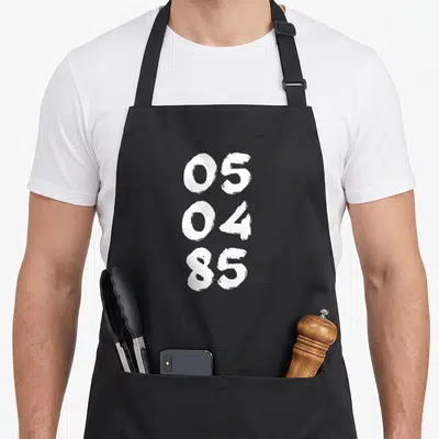 Tablier de cuisine noir avec les chiffres 05, 04 et 85 imprimés en blanc vertical.
