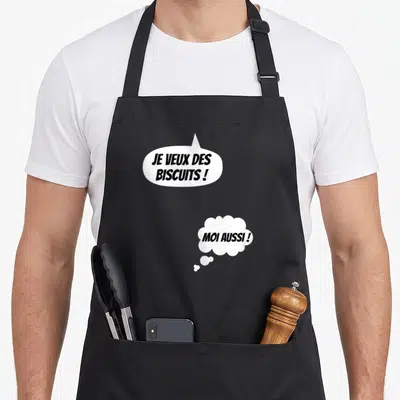 Tablier de cuisine noir avec bulles blanches contenant les textes Je veux des biscuits et Moi aussi en lettres noires.