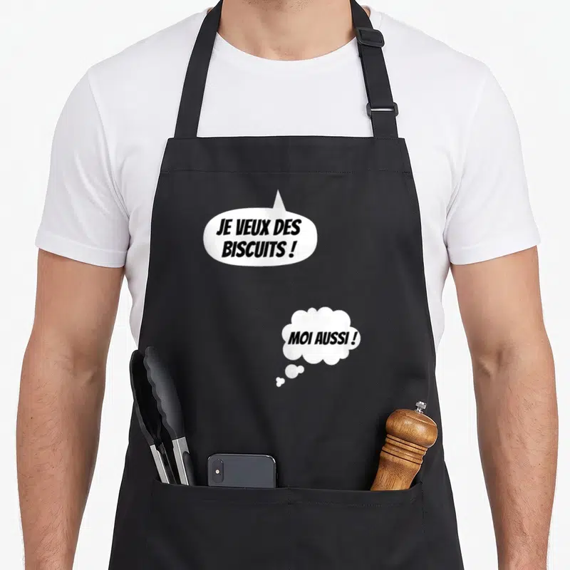Tablier de cuisine noir avec bulles blanches contenant les textes Je veux des biscuits et Moi aussi en lettres noires.