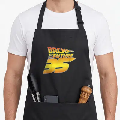 Tablier de cuisine noir avec le logo doré et orange Back to the Future 35 imprimé au centre.